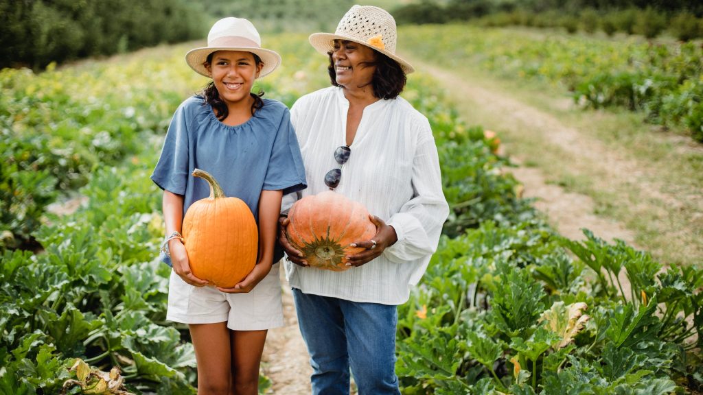 Happy Hispanic woman with daughter holding pumpkins